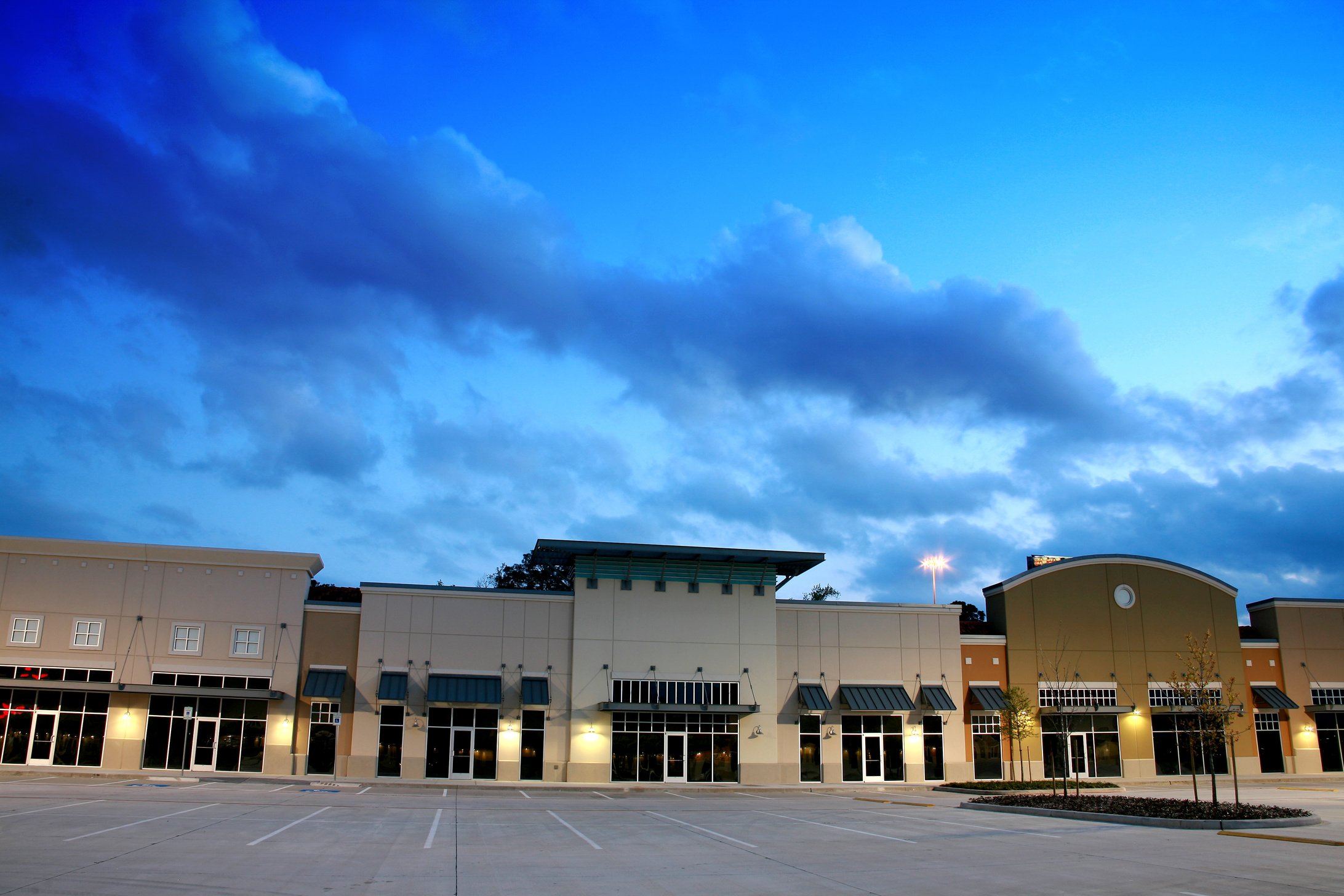 Empty new strip mall, shopping center buildings. Dusk, parking lot.